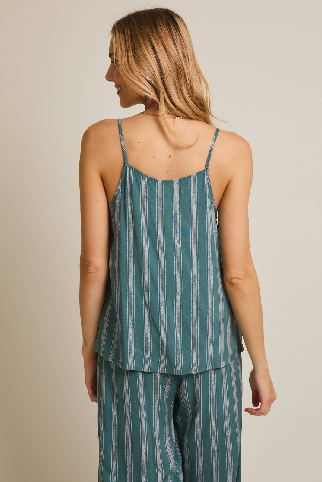 Woman wearing green and cream striped spaghetti strap top on gray background