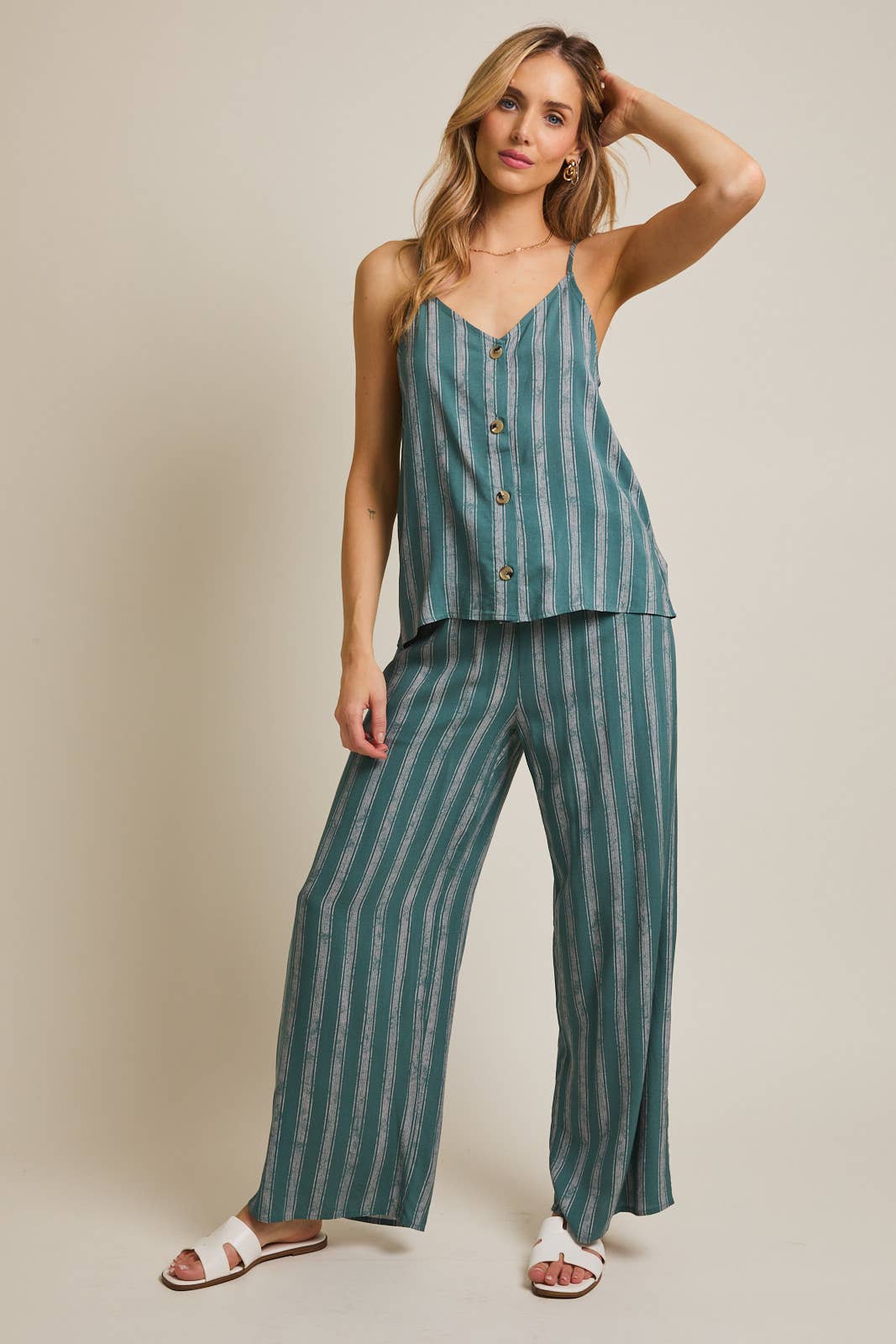 Woman wearing green and cream striped spaghetti strap top and matching pants on gray background
