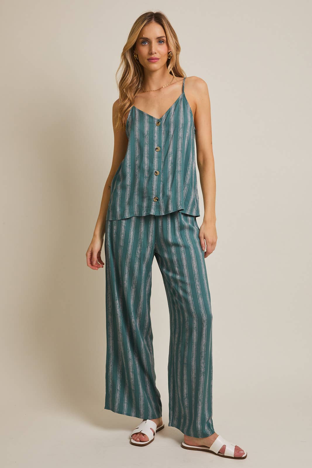 Woman wearing green and cream striped spaghetti strap top and matching pants on gray background