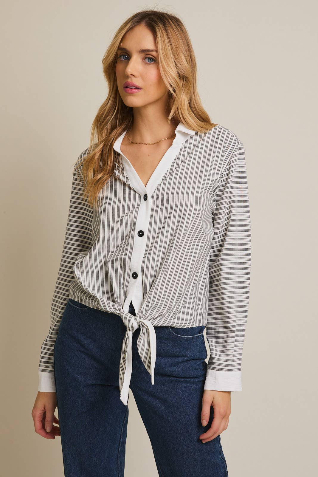 Woman wearing a striped shirt and blue pants against a beige background