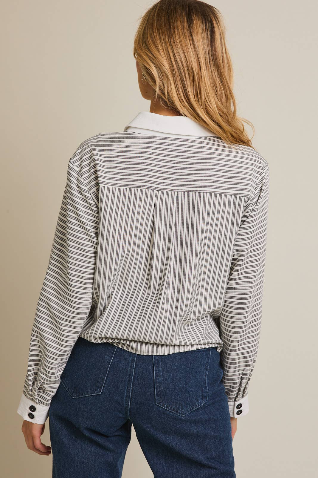 Woman wearing a striped shirt and blue pants against a beige 