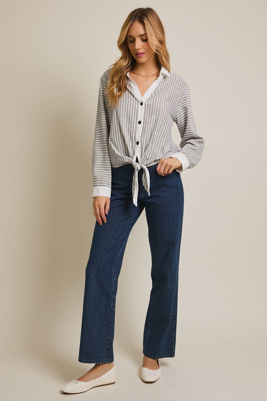 Woman wearing a striped shirt and blue pants against a beige 