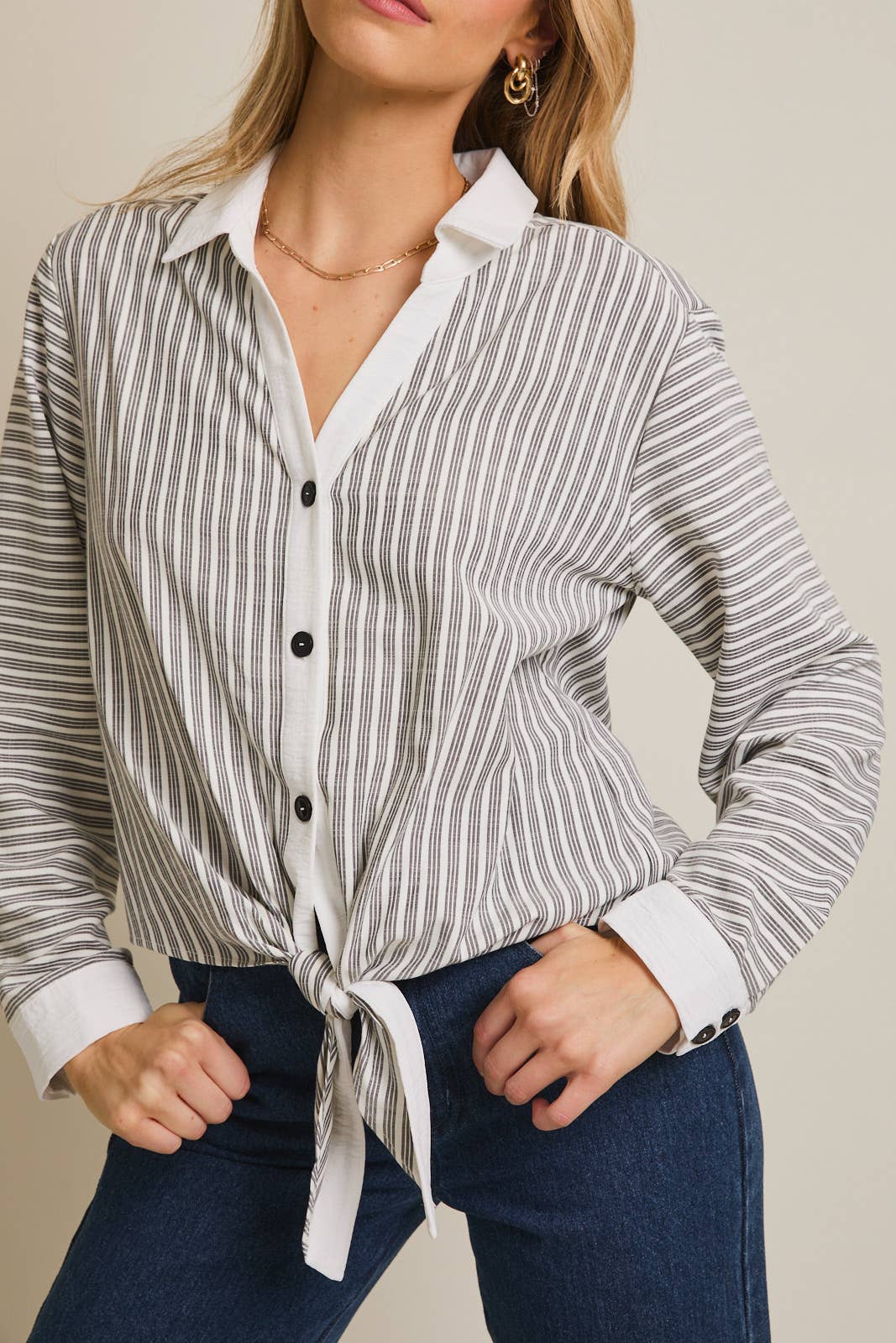 Woman wearing a striped shirt and blue pants against a beige 