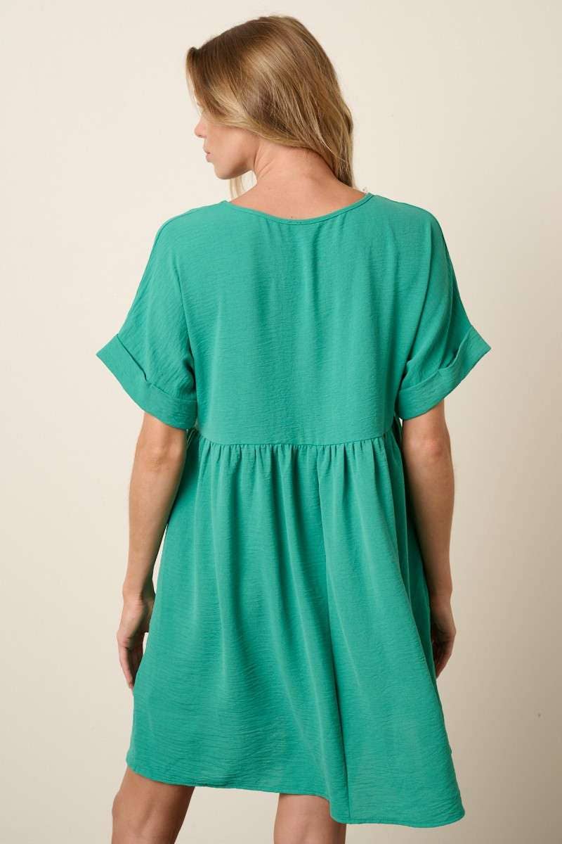 Back view of a woman wearing a green babydoll dress against a beige background