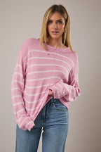 Woman wearing a pink and light pink striped sweater with blue jeans against a plain background