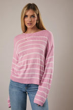 Woman wearing a pink and light pink striped sweater with blue jeans against a plain background