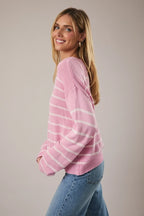 Woman wearing a pink and light pink striped sweater with blue jeans against a plain background