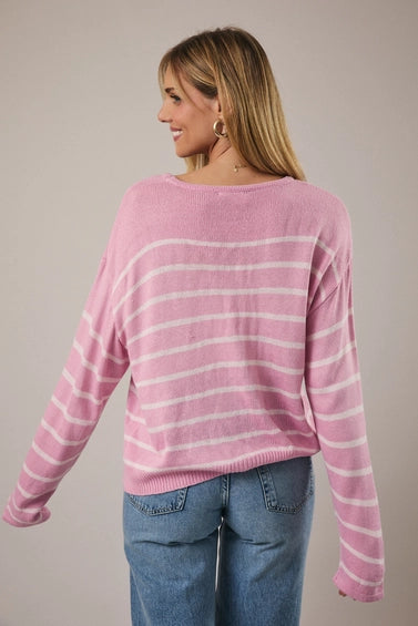 Back view of a woman wearing a pink and light pink striped sweater with blue jeans against a plain background