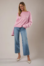 Woman wearing a pink and light pink striped sweater with blue jeans against a plain background