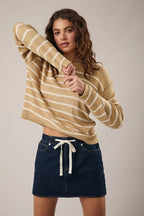 Woman wearing a tan and cream striped sweater with navy skirt against a plain background
