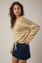 Woman wearing a tan and cream striped sweater with navy skirt against a plain background