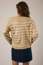Back view of a woman wearing a tan and cream striped sweater with navy skirt against a plain background