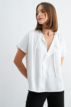 Woman wearing a white blouse with split neck on a plain background