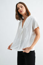 Woman wearing a white blouse with split neck on a plain background