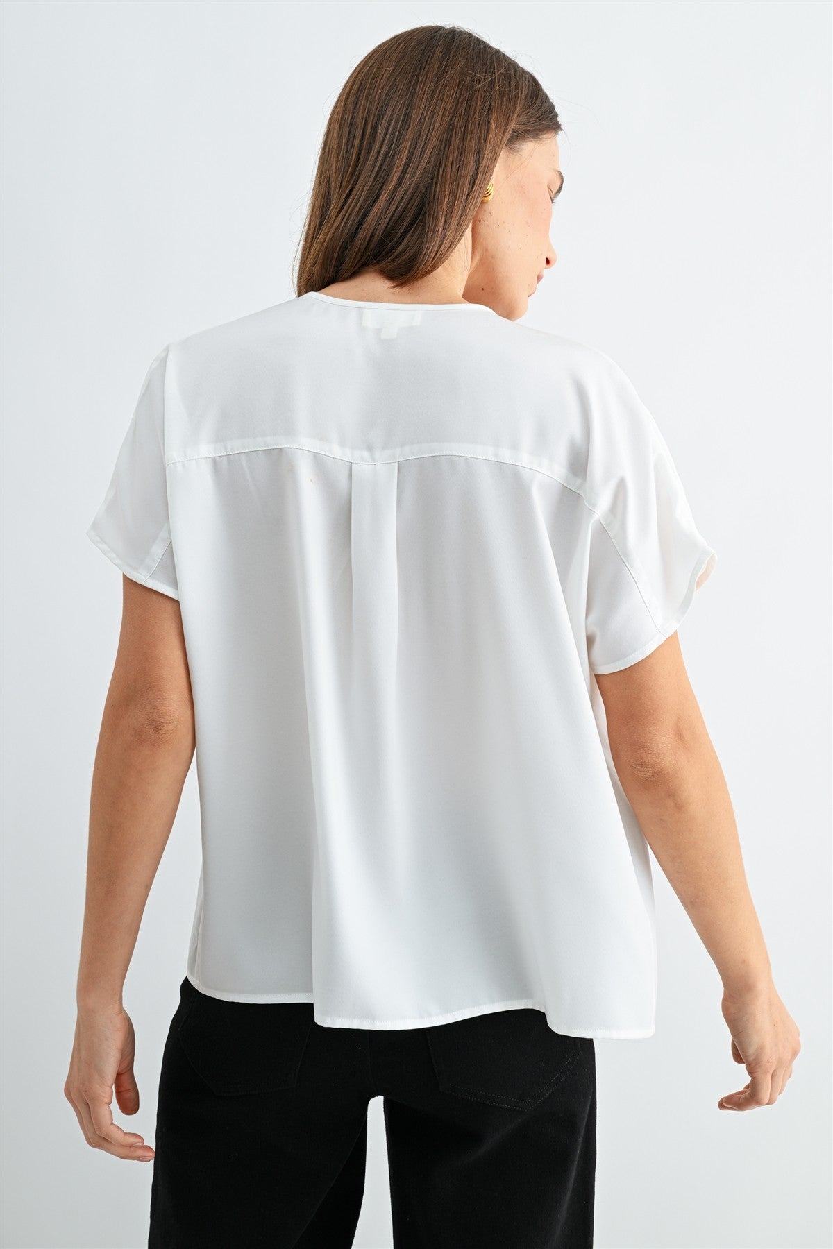 Back view of a woman wearing a white blouse with split neck on a plain background