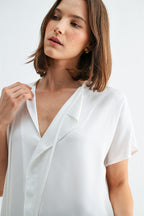 Woman wearing a white blouse with split neck on a plain background