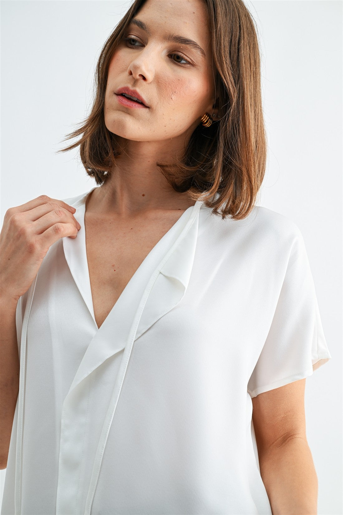 Woman wearing a white blouse with split neck on a plain background