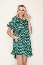 A woman modeling a short puff sleeve green dress with a white embroidered design, standing against a plain off-white background.