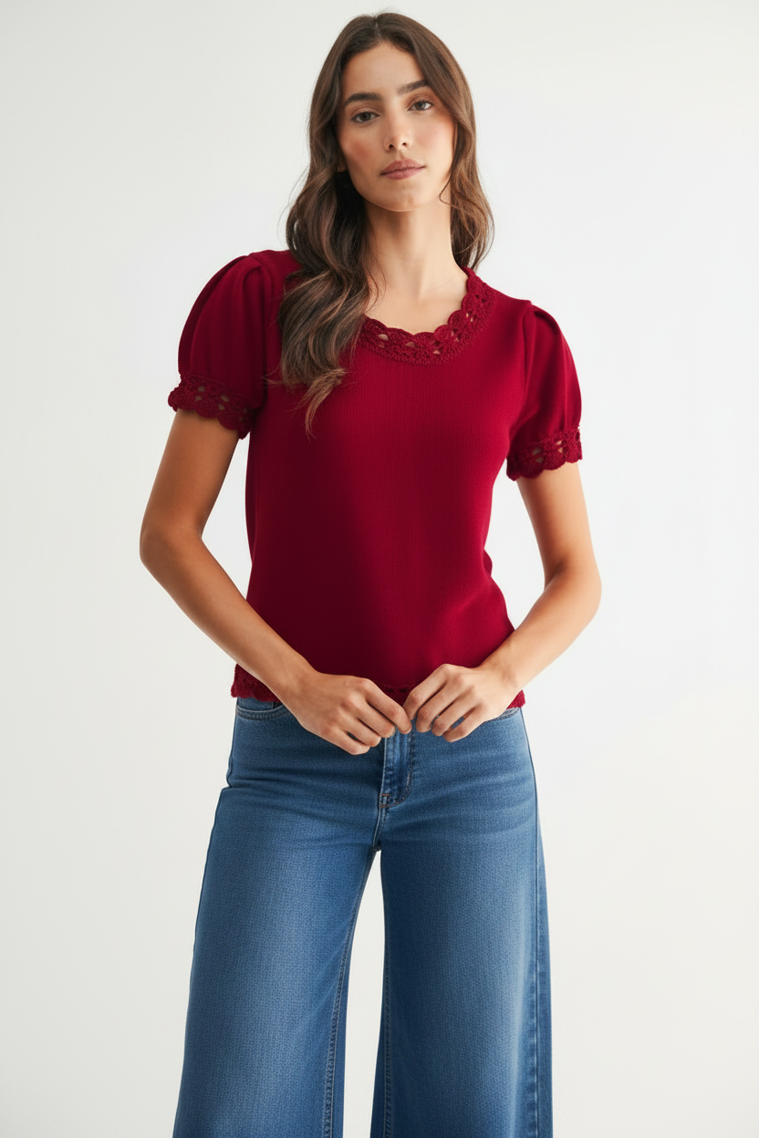 A woman modeling a short-sleeve red sweater with scallop crochet trim at the neckline, sleeve cuffs, and hem paired with blue jeans, against a plain light background.