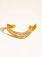 A gold-toned non-tarnish cuff bracelet with multiple parallel curved bands on a plain background