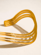 A gold-toned non-tarnish cuff bracelet with multiple parallel curved bands on a plain background