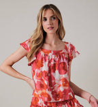 Woman wearing an orange and pink floral top against a plain background