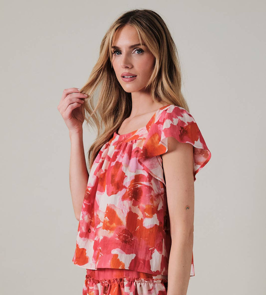 Woman wearing an orange and pink floral top against a plain background