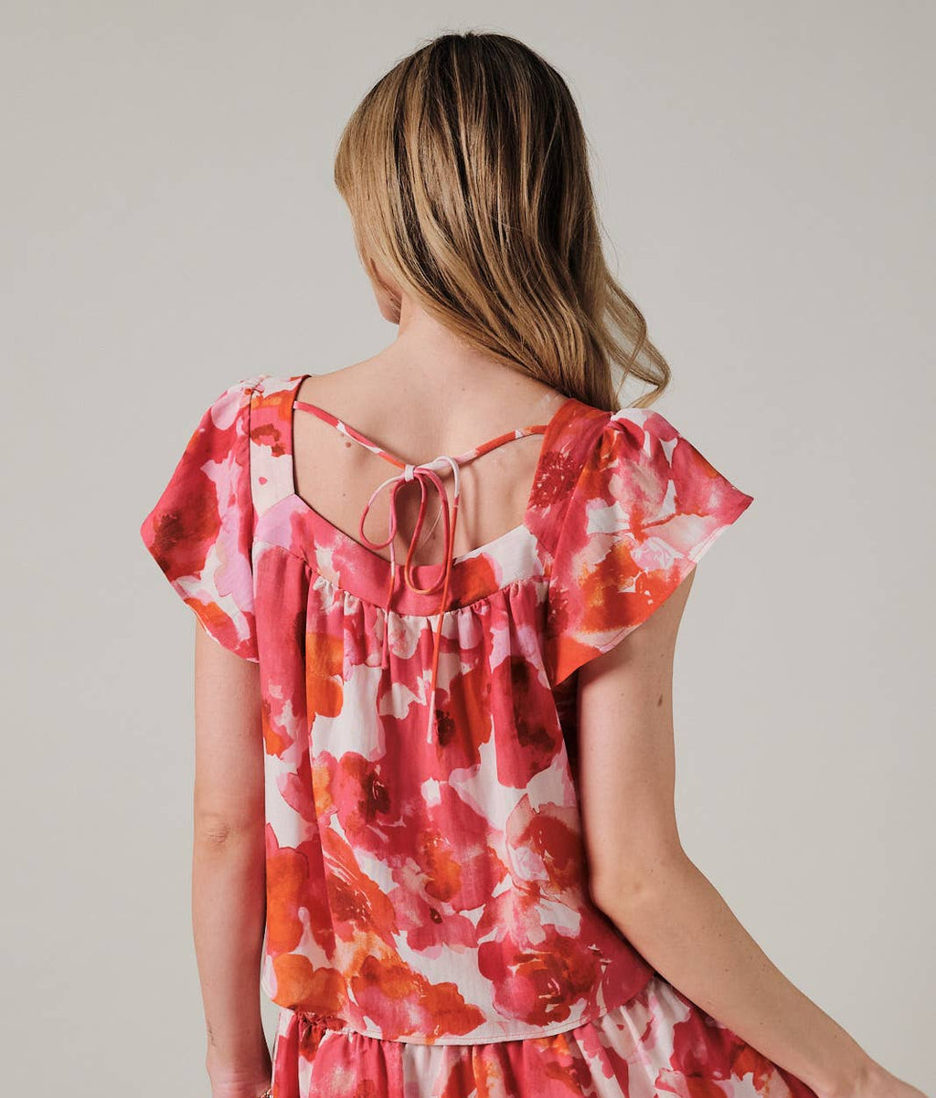 Back view of a woman wearing an orange and pink floral top against a plain background