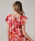 Back view of a woman wearing an orange and pink floral top against a plain background