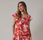 Woman wearing an orange and pink floral top against a plain background