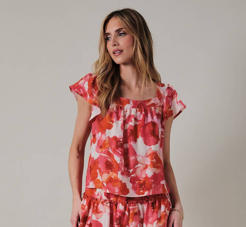 Woman wearing an orange and pink floral top against a plain background