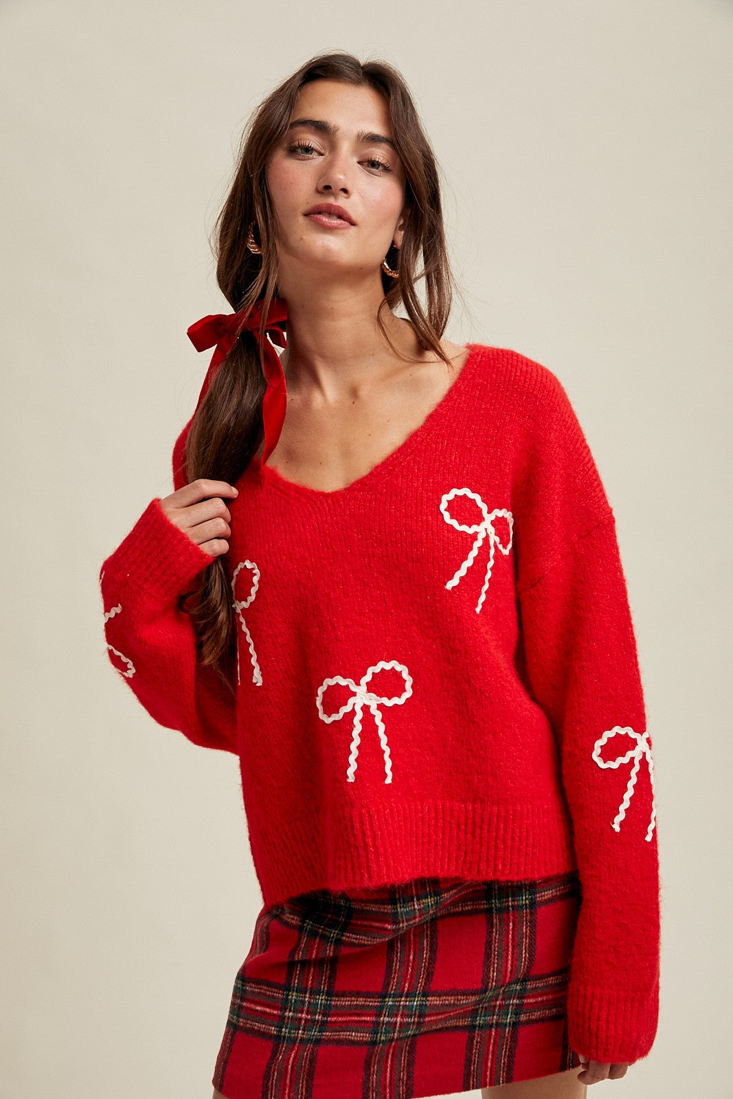 Woman wearing a red sweater with white rick rack bow patterns and plaid skirt on a beige background