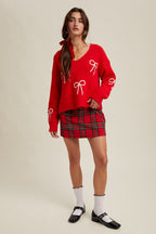 Woman wearing a red sweater with white rick rack bow patterns and plaid skirt on a beige background