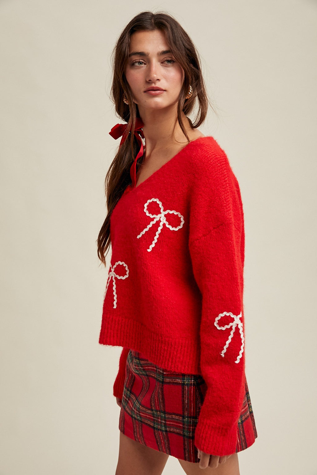 Woman wearing a red sweater with white rick rack bow patterns and plaid skirt on a beige background