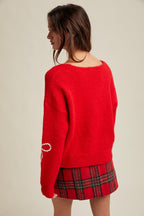 Back view of a woman wearing a red sweater with white rick rack bow patterns and plaid skirt on a beige background