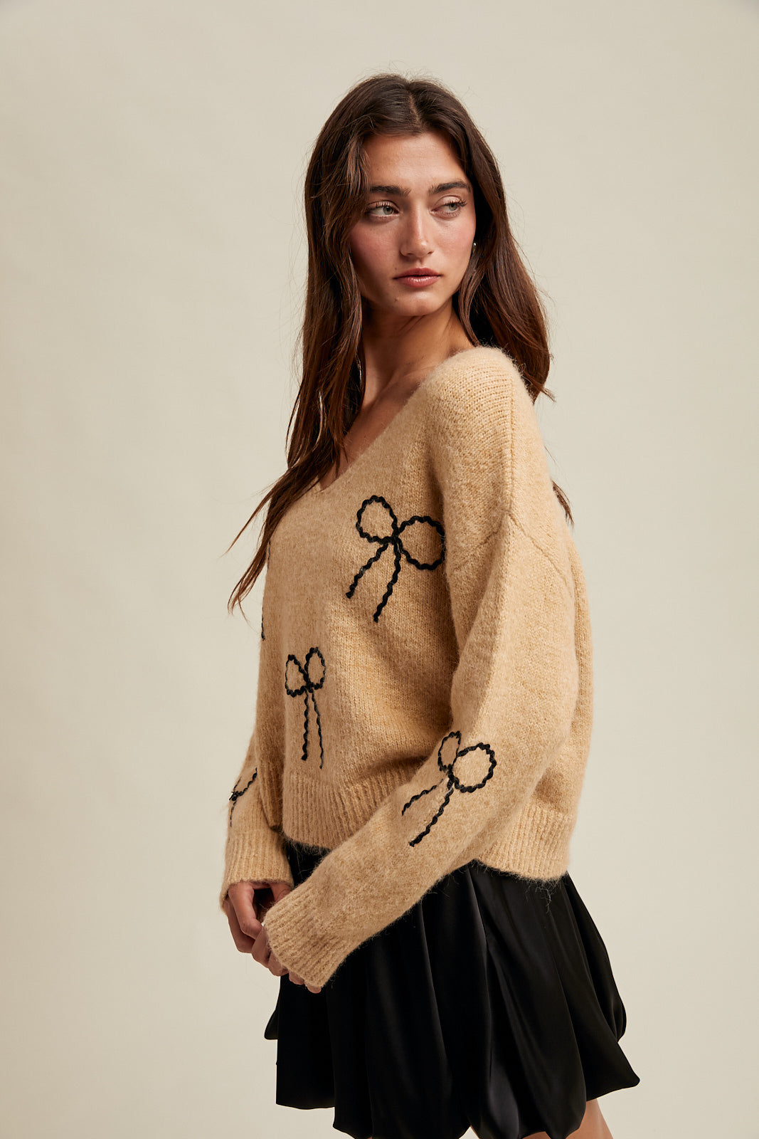 Woman wearing a taupe sweater with black rick rack bow designs and black skirt on a neutral background