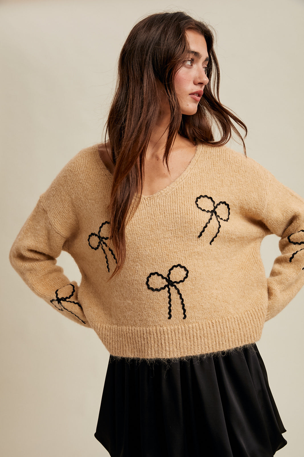 Woman wearing a taupe sweater with black rick rack bow designs on a neutral background