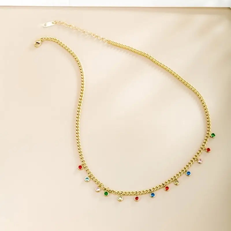 Gold chain necklace with colorful gemstones on a beige surface