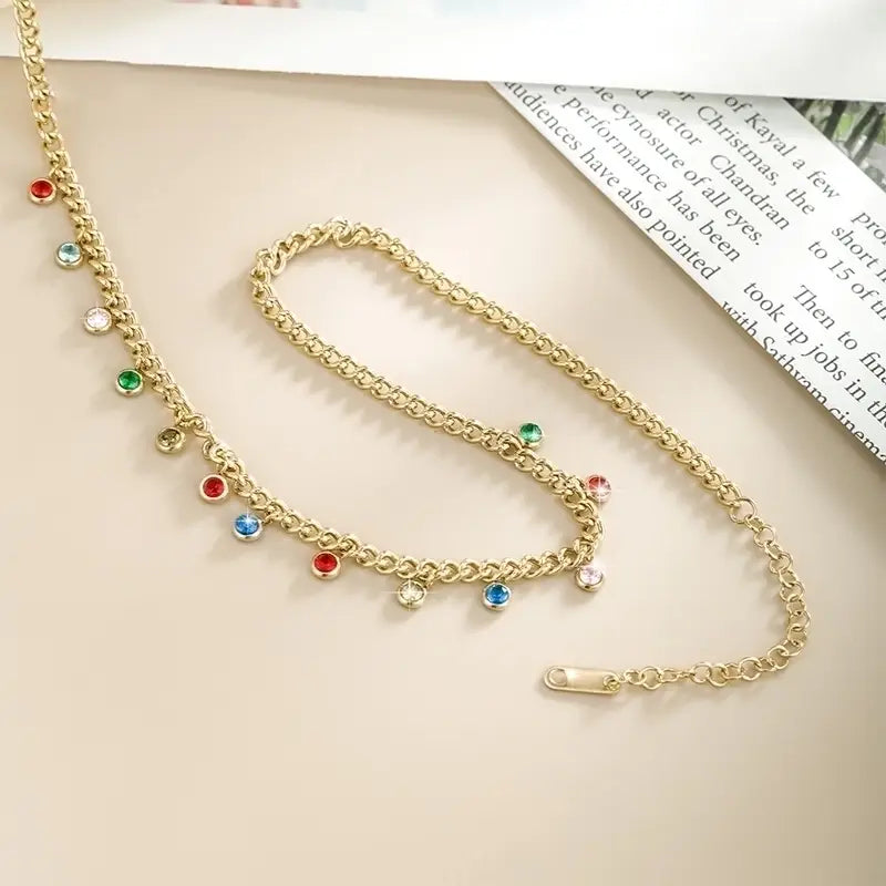 Gold chain necklace with colorful gemstones on a beige surface