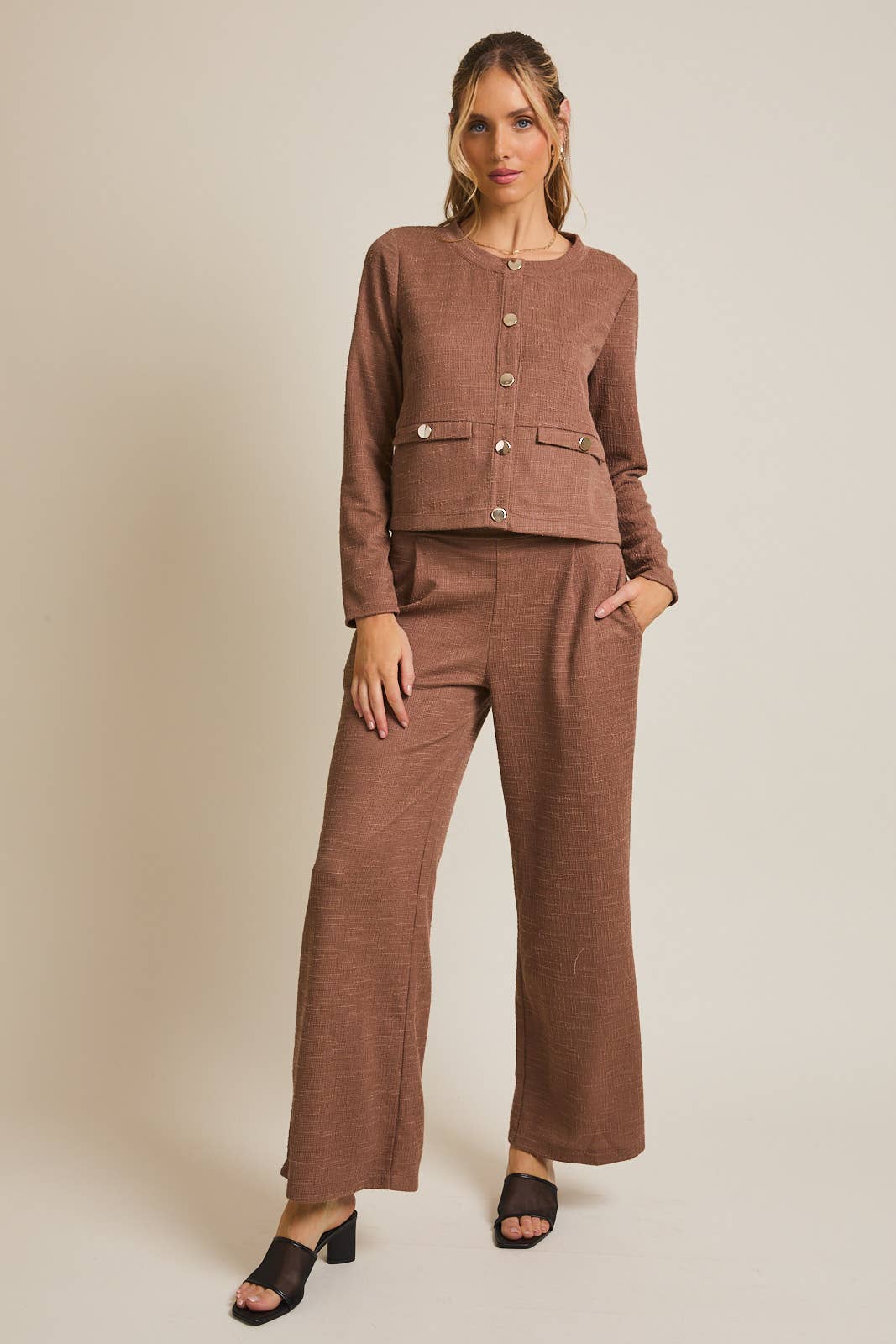 Woman wearing a brown boucle outfit with a jacket and wide-leg pants on a beige background