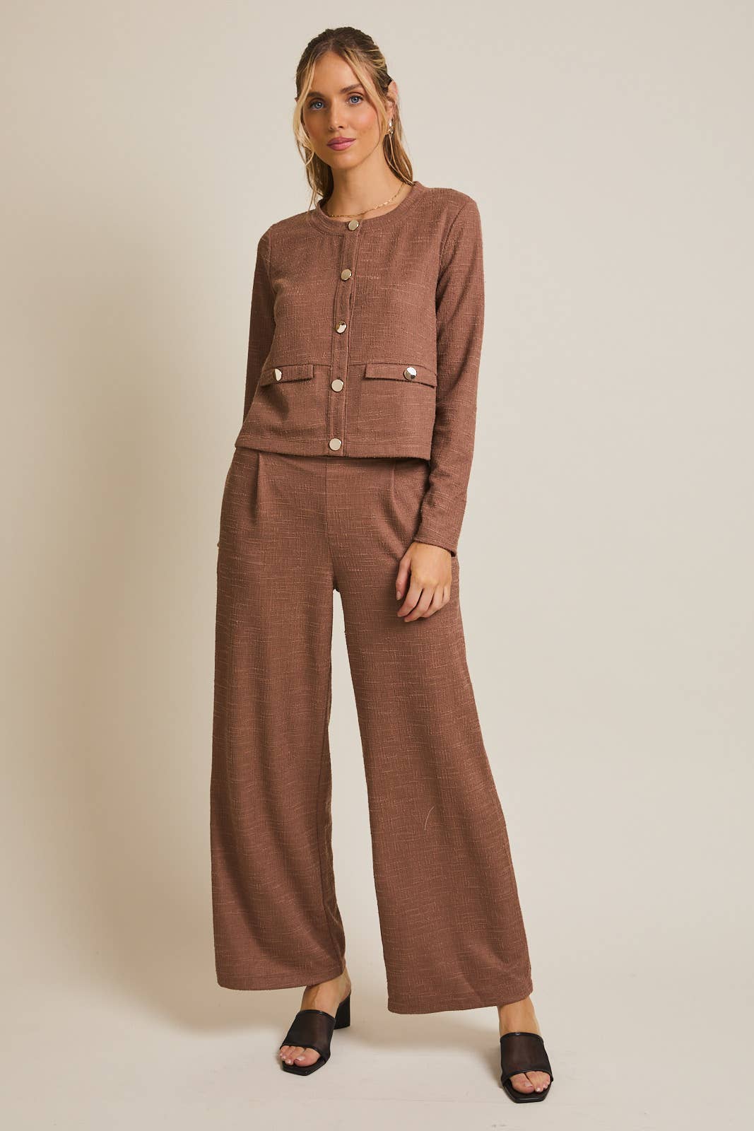 Woman wearing a brown boucle outfit with wide-leg pants and a cropped jacket on a beige background