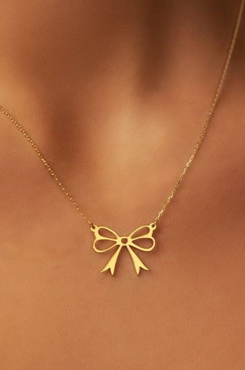 18k gold-plated stainless steel bow-shaped necklace on a woman's neck against a brown background