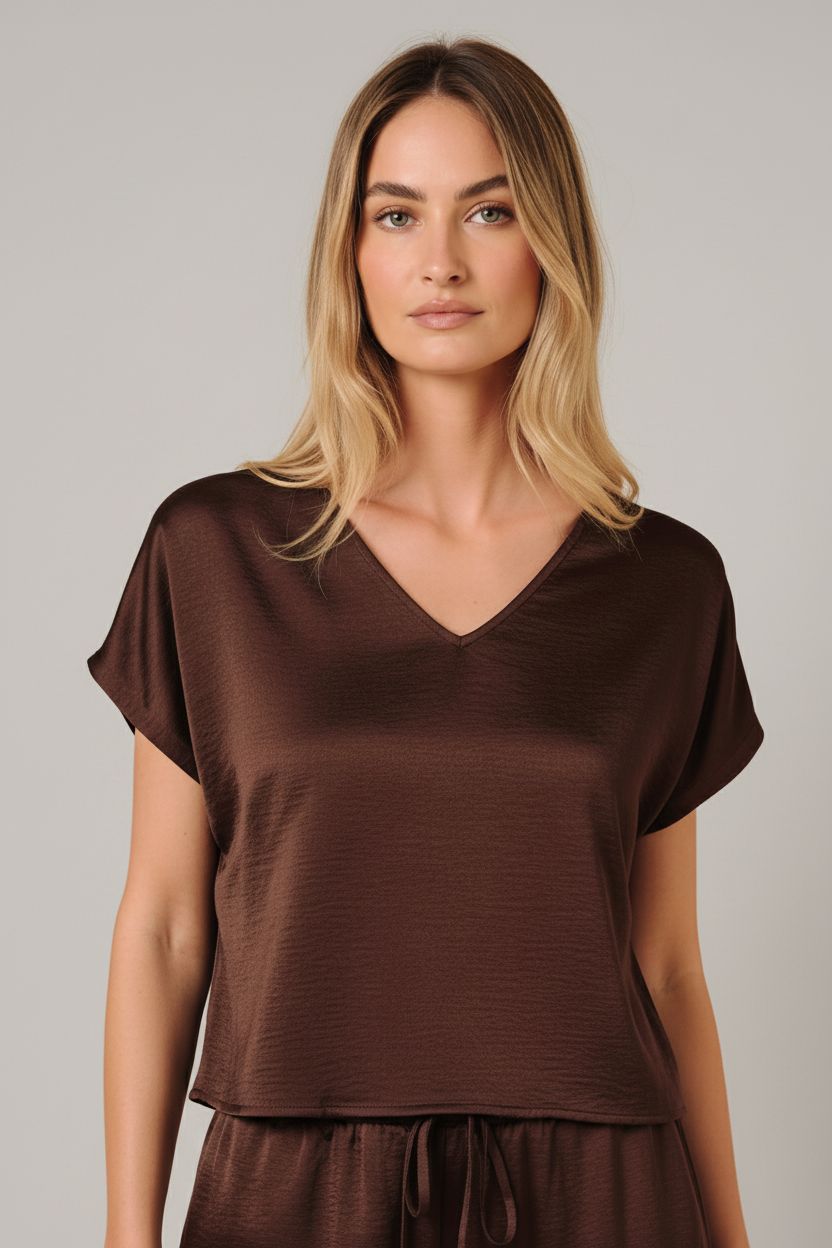 A woman modeling a brown crinkle satin top with dolman short sleeve and V-neckline against a solid beige background.