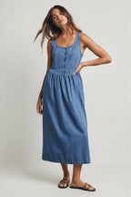 Woman wearing a medium blue denim tank dress against a gray 
background