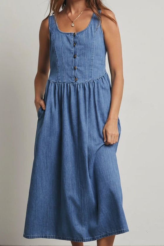 Woman wearing a medium blue denim tank dress against a gray 
background