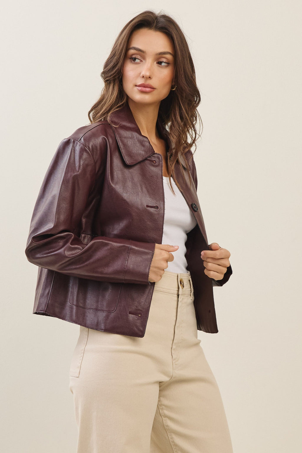Woman wearing a burgundy faux leather jacket and beige pants on a plain background