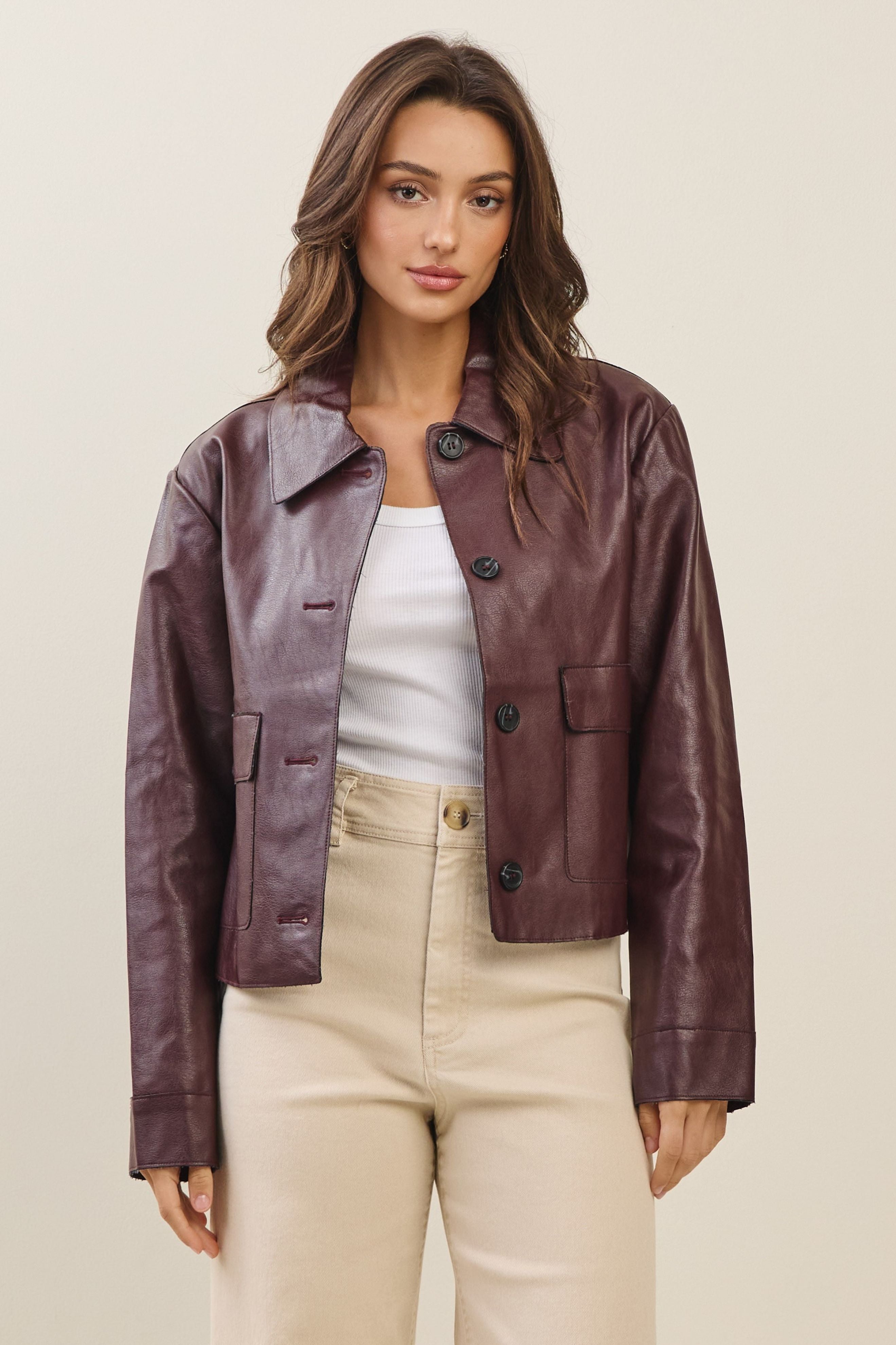 Woman wearing a burgundy faux leather jacket and beige pants on a plain background
