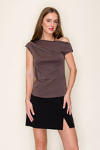 A woman modeling a brown scuba drape one shoulder top paired with a black skirt, standing against a plain off-white background.