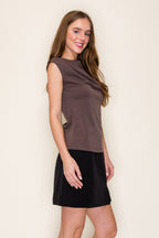 A woman modeling a brown scuba drape one shoulder top paired with a black skirt, standing against a plain off-white background.
