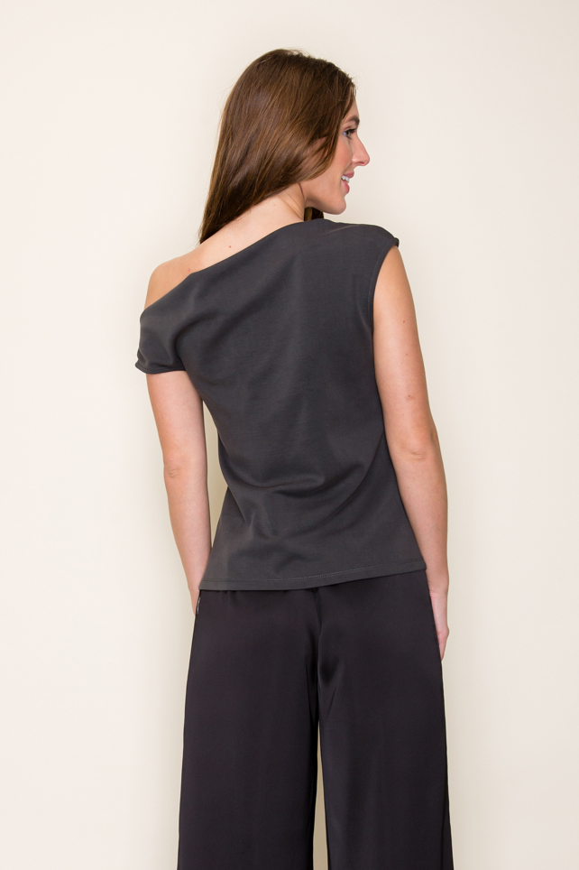 A woman shown from the back wearing a dark grey scube drape one shoulder modal top and black wide-leg pants, standing against a plain off-white background.